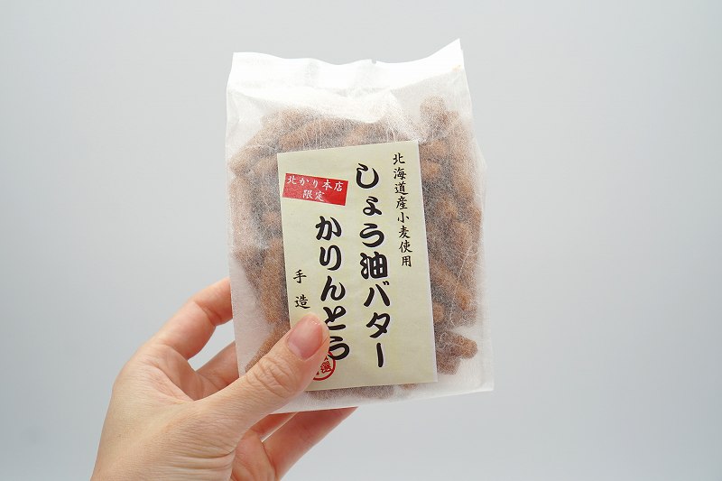 北かり本店限定品「しょう油バターかりんとう」の袋を手に持っている様子