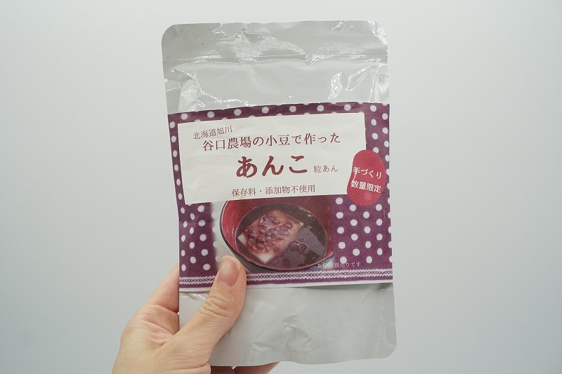 「谷口農場の小豆でつくった 粒あん 300g（税込486円）」を手に持っている様子