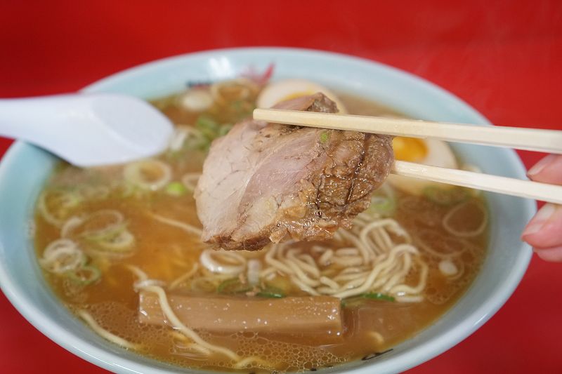 梅光軒 旭川本店の醤油ラーメンのチャーシューを箸で持ち上げている様子