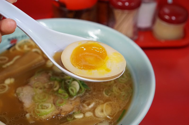 梅光軒 旭川本店の醬油ラーメンに入っている味玉を、れんげで持ち上げている様子