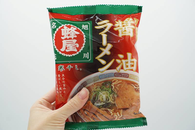 「蜂屋 寒干しラーメン 醤油味・一人前（税込330円）」を手に持っている様子