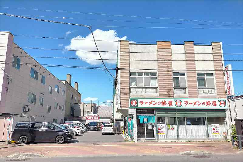 白地に赤と緑の看板をかかげる「ラーメンの蜂屋本店」の外観