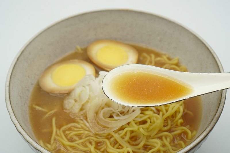 梅光軒の袋ラーメンのスープをれんげですくっている様子